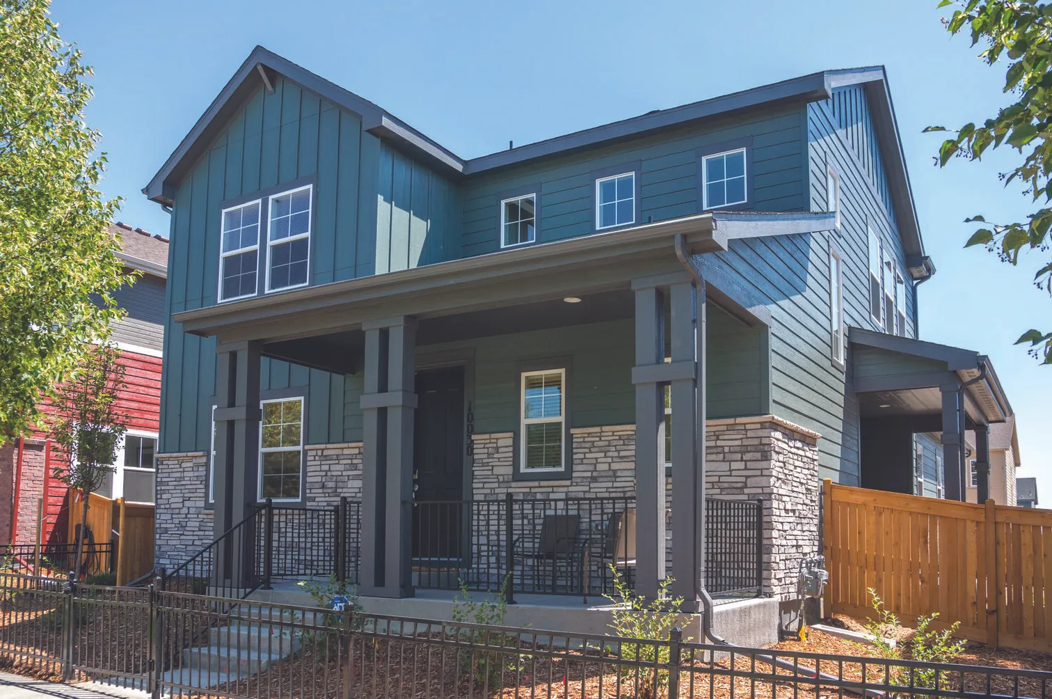 Two-story modern house with green siding, stone accents, a covered front porch, and black railing.